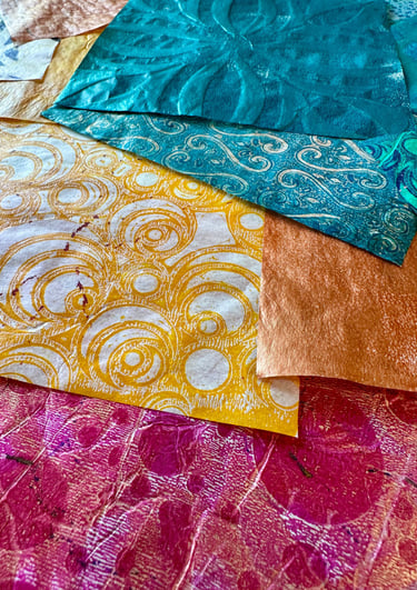 Stack of hand-painted collage papers with gold pattern and vibrant colors