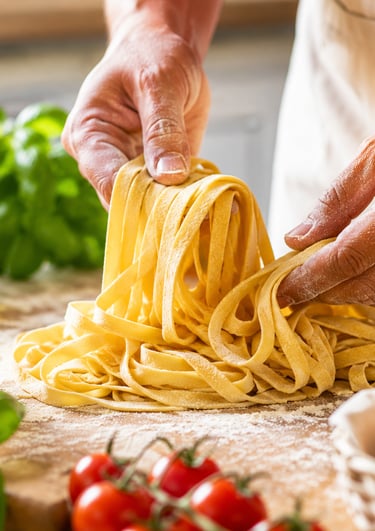 Chef making fresh homemade pasta noodles by hand on a wooden table with flour, eggs, and basil.