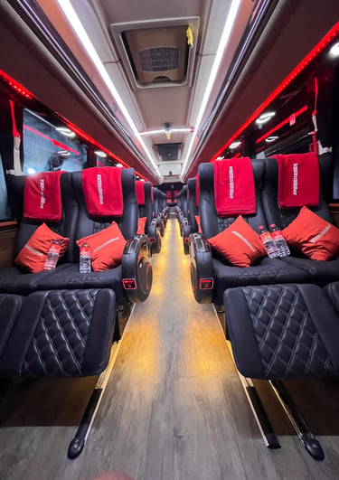 Luxury tour bus interior featuring black leather recliner seats, orange pillows, and red ambient lighting.