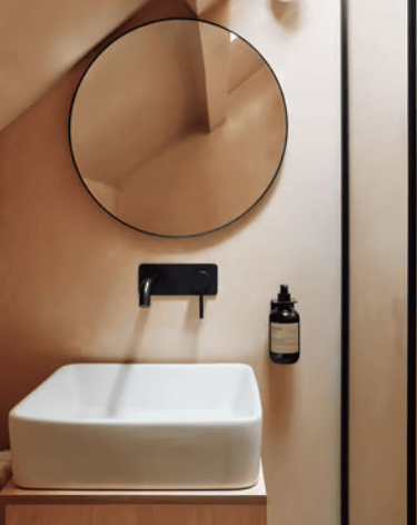Modern bathroom vanity featuring a white vessel sink, matte black faucet, and a round wall mirror.