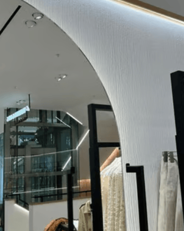 Modern luxury clothing store interior featuring a minimalist textured archway and designer apparel on black display racks.