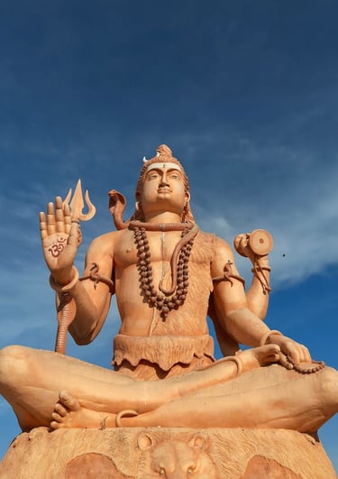 Giant statue of Hindu Lord Shiva in a meditative yoga pose with a trident and cobra against a blue sky.
