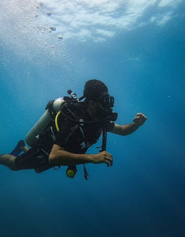 A scuba diver swimming through deep blue ocean water with sun rays and air bubbles.