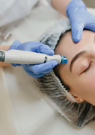 Esthetician performing a professional hydrafacial treatment on a woman's forehead for skin rejuvenation.