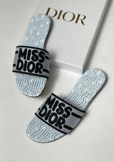 Luxury Miss Dior flat slides in light blue and black embroidery next to a designer shoe box.
