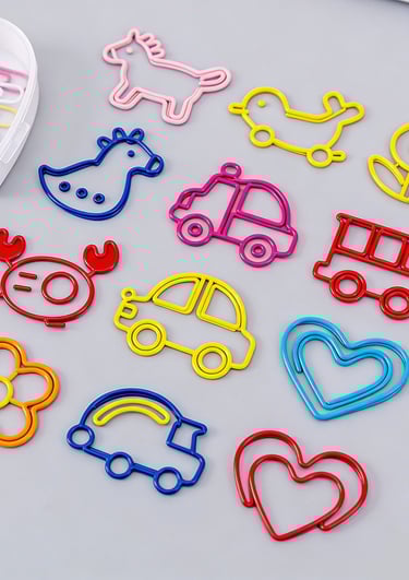 Collection of colorful novelty paper clips in shapes like animals, cars, hearts, and flowers on a grey surface.
