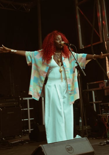 A female singer with vibrant red hair performs live on stage wearing a colorful patterned shirt.