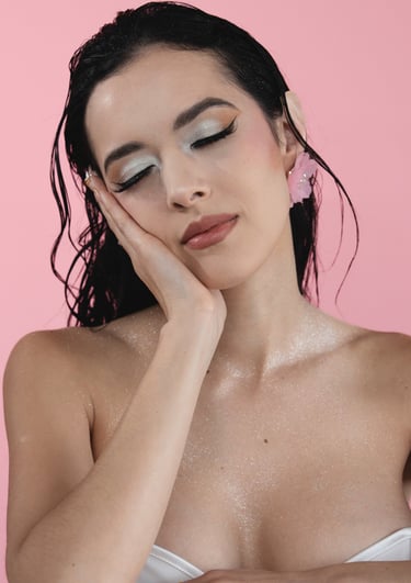 Woman with wet hair and silver glitter makeup posing against a pink background.