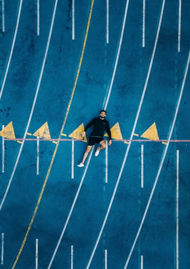 Aerial view of a male athlete lying on a blue running track with white lane lines.