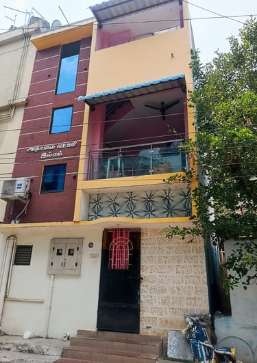 Three-story residential building with a balcony, yellow and maroon facade, and blue tinted windows.