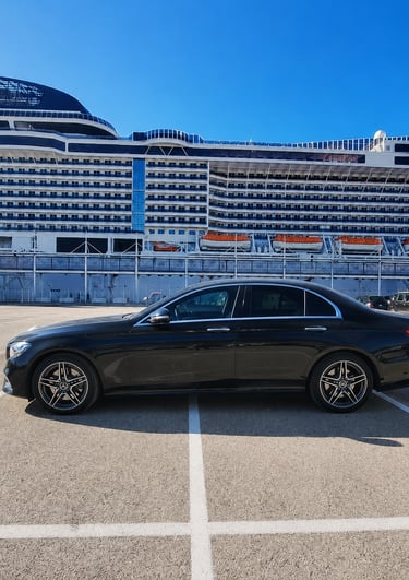 Black Mercedes-Benz luxury sedan parked at a cruise ship terminal under a clear blue sky.