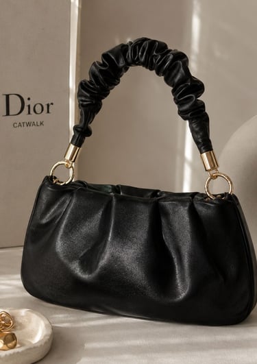 Black ruched shoulder bag with gold hardware styled in a beige luxury aesthetic.