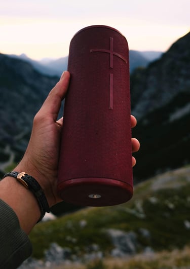 a person holding a red bluetooth speaker in their hand overlooking a mountain
