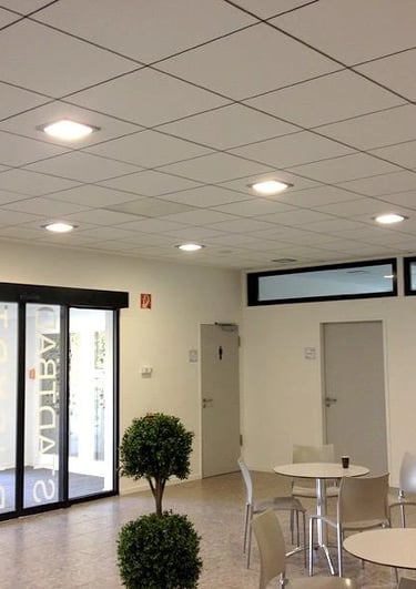 Sufit kasetonowy w biurze, białe kasetony z wbudowanymi lampami LED, minimalistyczne wnętrze z oknami i stolikami.