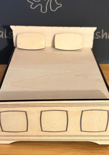 Small wooden miniature bed with headboard and pillows. 