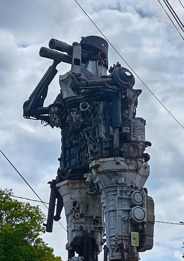 Tall steampunk robot sculpture made from recycled car engines and mechanical scrap metal parts.