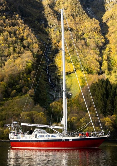 a sailboat in Norway in the water with a waterfall in the background | Sailing adventures in Norway