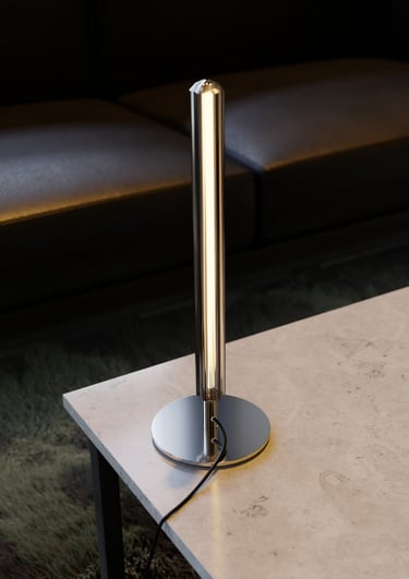 Lampe design chromée posée sur une table en pierre claire devant un canapé noir, rendu 3D moderne et minimaliste.