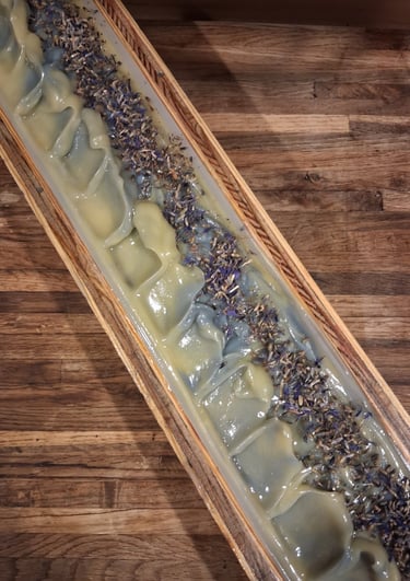 Handmade Blue soap loaf in a wooden mold topped with dried botanical flower buds on a rustic table.