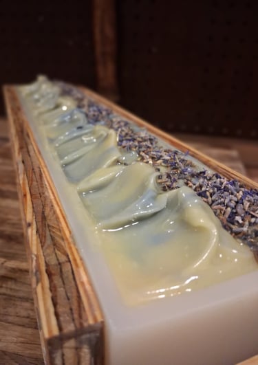 Handmade bluebird lane soap loaf in a wooden mold topped with dried botanical flower buds.