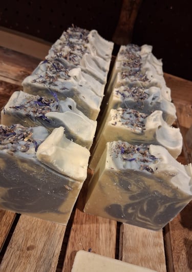 Handmade soap bars with swirls of grey and white topped with dried botanical flowers on a wooden tray.