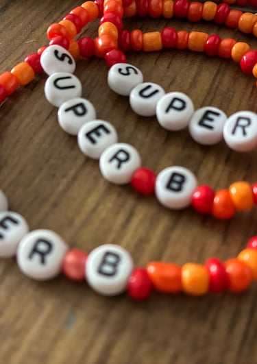 Handmade red and orange beaded friendship bracelets with white letter beads spelling SUPER B.