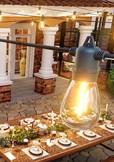 Warm outdoor string lights hanging over an elegant patio dining table set for a garden dinner party.