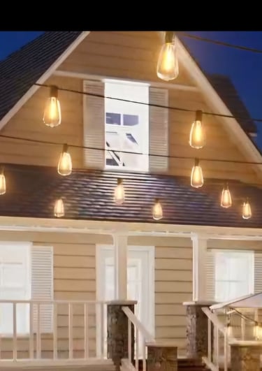 Warm outdoor string lights hanging over a cozy house porch and patio at dusk for backyard lighting decor.