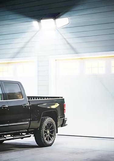 Solar powered motion sensor outdoor security light illuminating a driveway and black pickup truck at night.