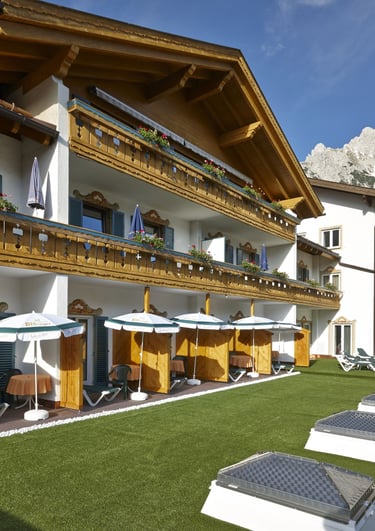 Luxury alpine hotel with wooden balconies and green lawn against a mountain backdrop.
