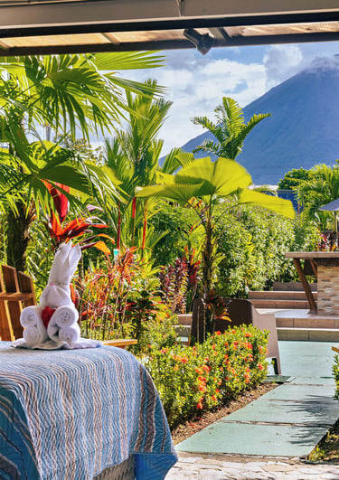 Luxury tropical resort bedroom view of Arenal Volcano through sliding doors with palm trees.