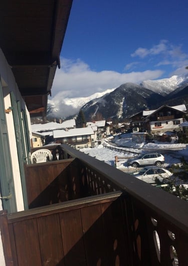A sunny balcony view of a snowy mountain village with alpine chalets and winter scenery.