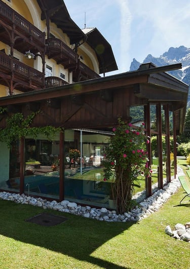 Luxury alpine hotel with an indoor pool and sun loungers on a green lawn facing the Alps.