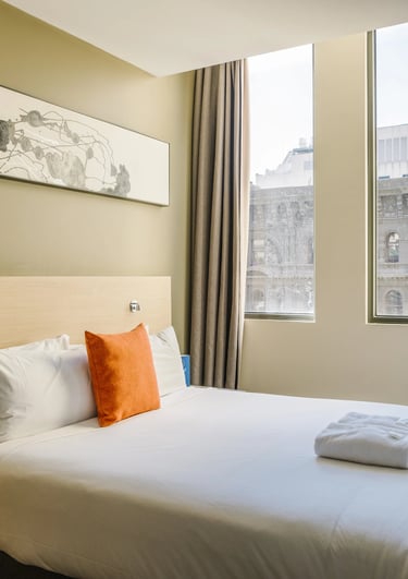 Habitación de hotel moderna con cama queen, sábanas blancas, cojín decorativo naranja