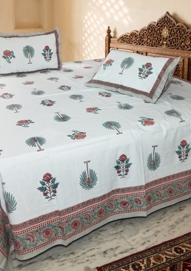 White block print cotton bedsheet with floral and palm tree motifs on a carved wooden bed.