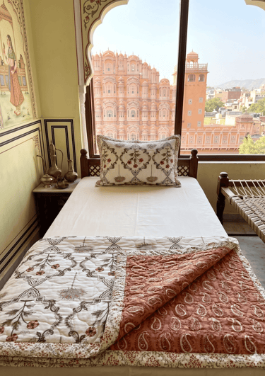 A boutique hotel bedroom in Jaipur featuring a view of the Hawa Mahal palace from the window.