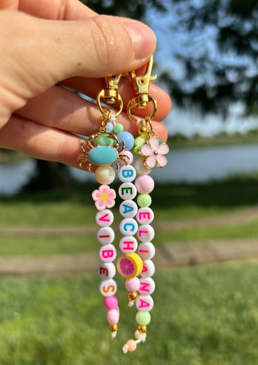 Mano sosteniendo dos llaveros, hecho de cuentas con letras y flores