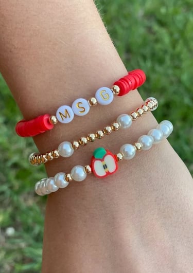 Pulseras colocadas en el brazo, con perlas, letras y un charm con figura de manzana