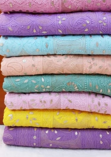 Stack of colorful Chikankari embroidered fabrics with sequins in pastel pink, blue, and yellow.
