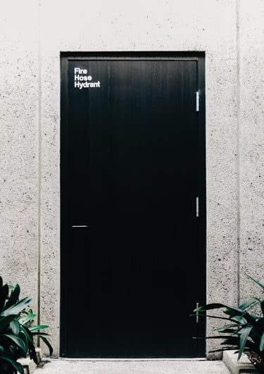 Foto a blanco y negro de una puerta negra cerrada al fondo de un pequeño pasillo.