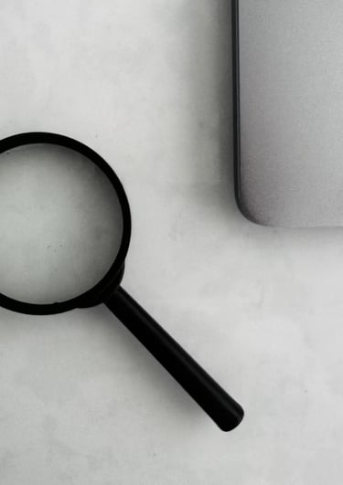 Foto a blanco y negro de una lupa y una laptop sobre un escritorio.