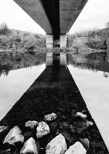 a bridge spanning a river with rocks and water and reflections
