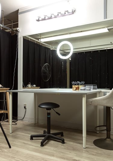 a room with a table and chairs and a fan and large mirror vanity for makeup