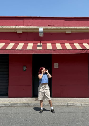 a girl standing in front of a red building. Una niña parada frente a un edificio rojo..