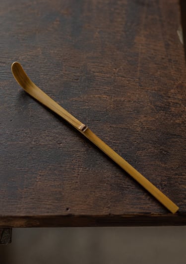 Handcrafted bamboo chashaku matcha tea scoop resting on a rustic dark wood table.