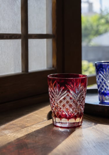 Red and blue Edo Kiriko cut glass tumblers on a wooden table by a traditional Japanese window.