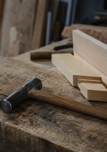 Vintage metal hammer laying on a rustic wooden workbench in a carpentry workshop.