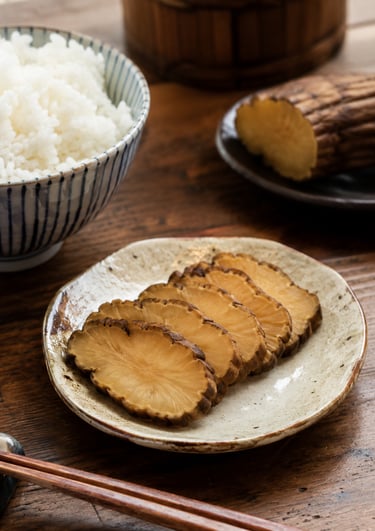 Sliced smoked iburigakko daikon radish pickles served on a ceramic plate with steamed white rice and chopsticks.