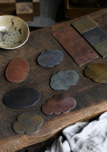 Handcrafted metal tea coasters in cloud and flower shapes on a rustic wooden table.