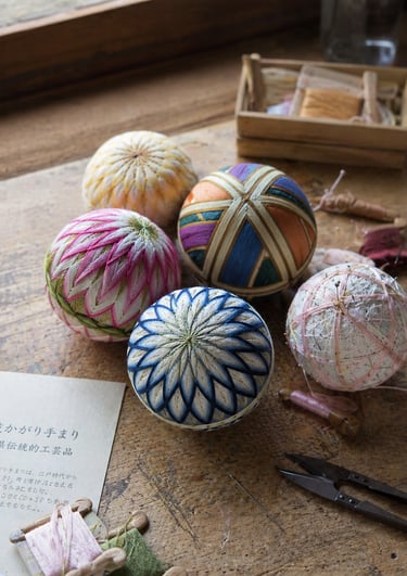 Handcrafted Japanese Temari balls with intricate embroidery on a rustic wooden table.